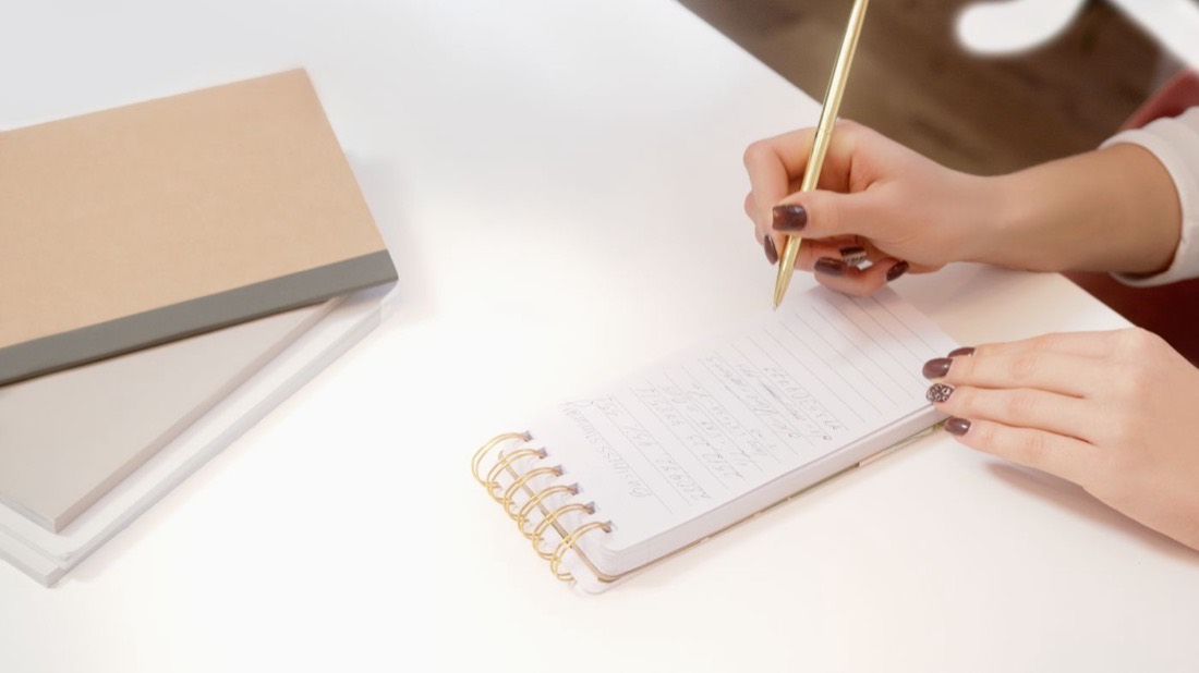 Hands writing in a notebook, illustrating how French scores convert to NCLC levels