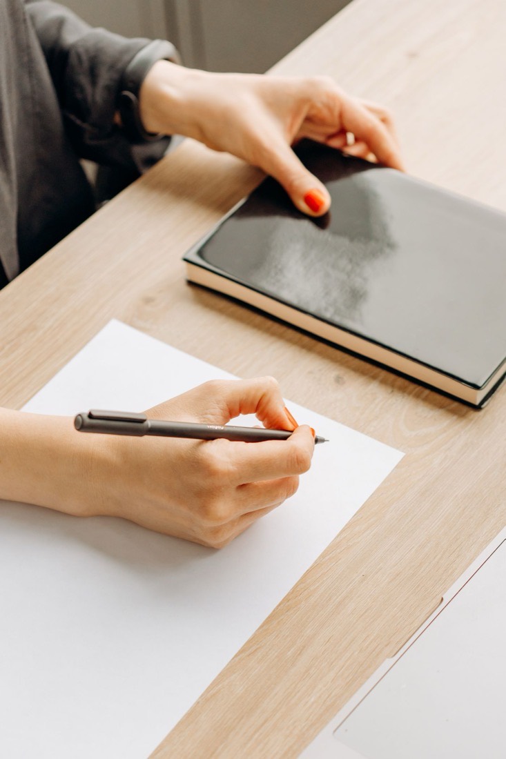 A hand writing on paper at a desk, illustrating the choice between passé composé and imparfait