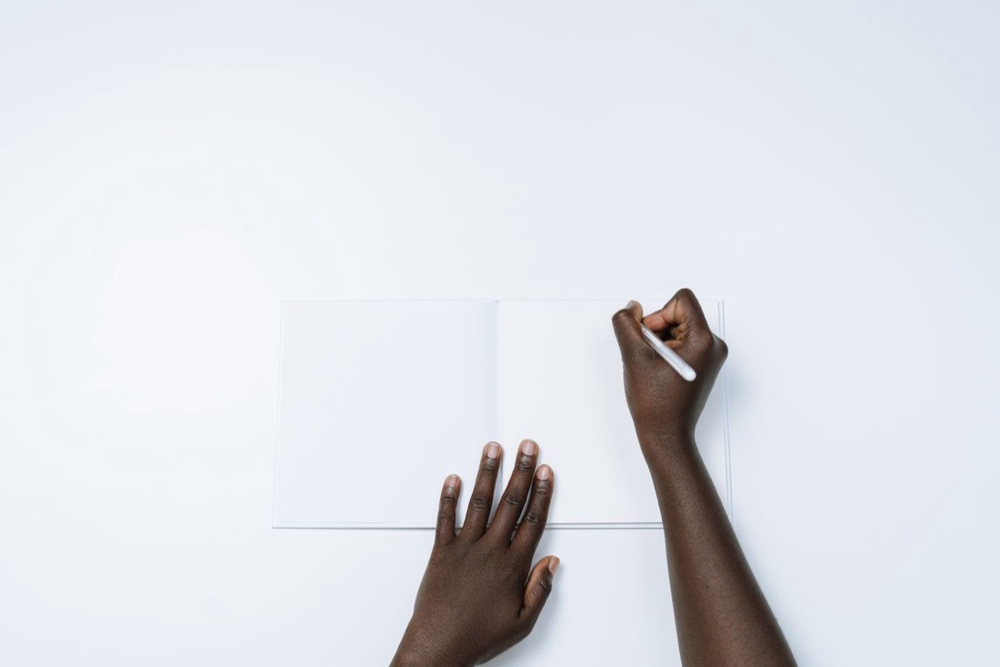 Hands writing on a blank notebook page, illustrating work on the French subjunctive